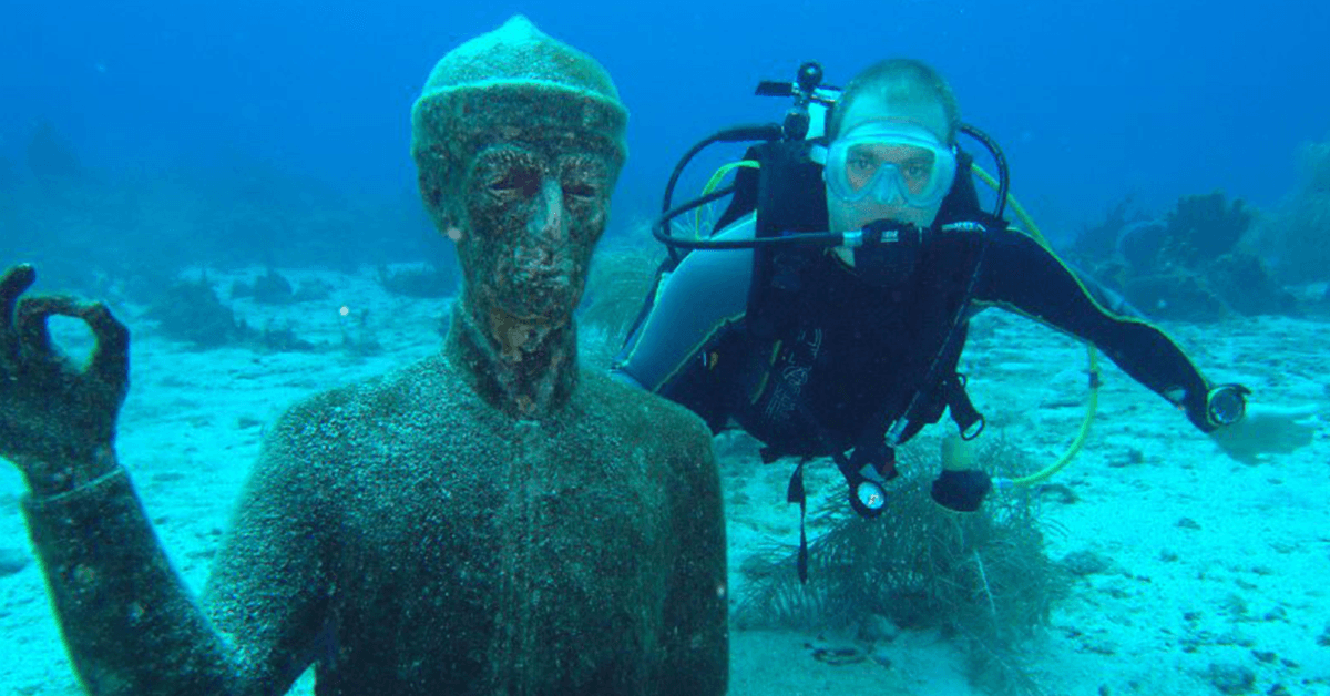 Diving in the Cousteau Marine Park is always a treat, here; this diver is taking the opportunity to be pictured with one of the Cousteau Underwater Statues in the reserve.